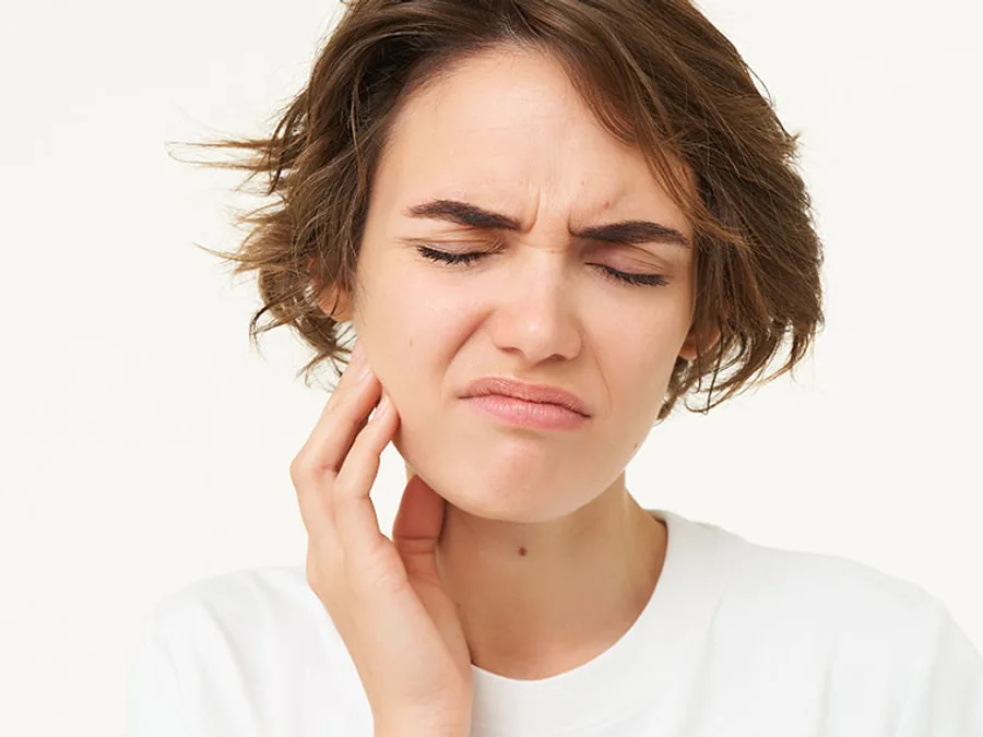 Woman wincing and holding the side of her jaw in pain
