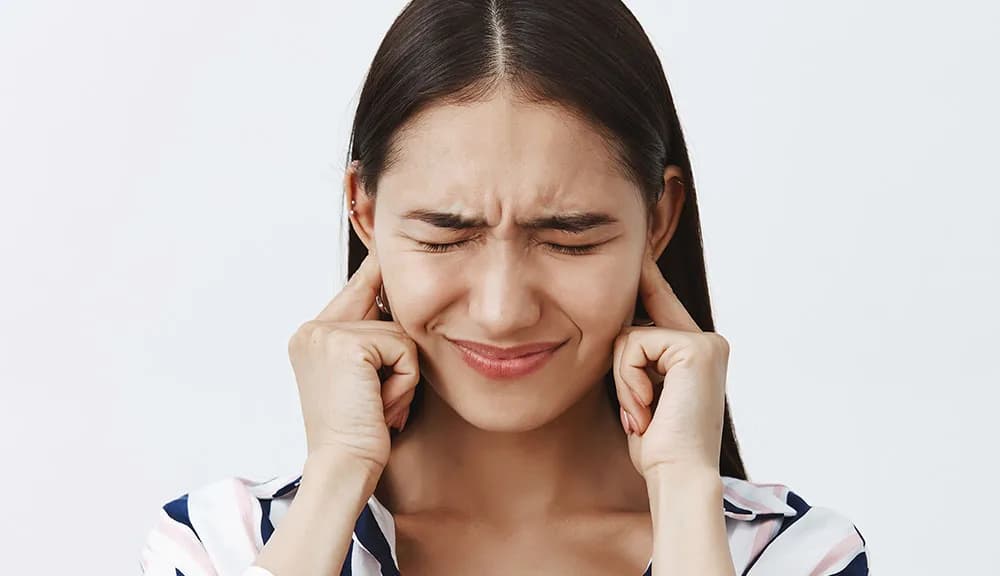 Woman pressing her knuckles to both jaw joints in TMJ pain