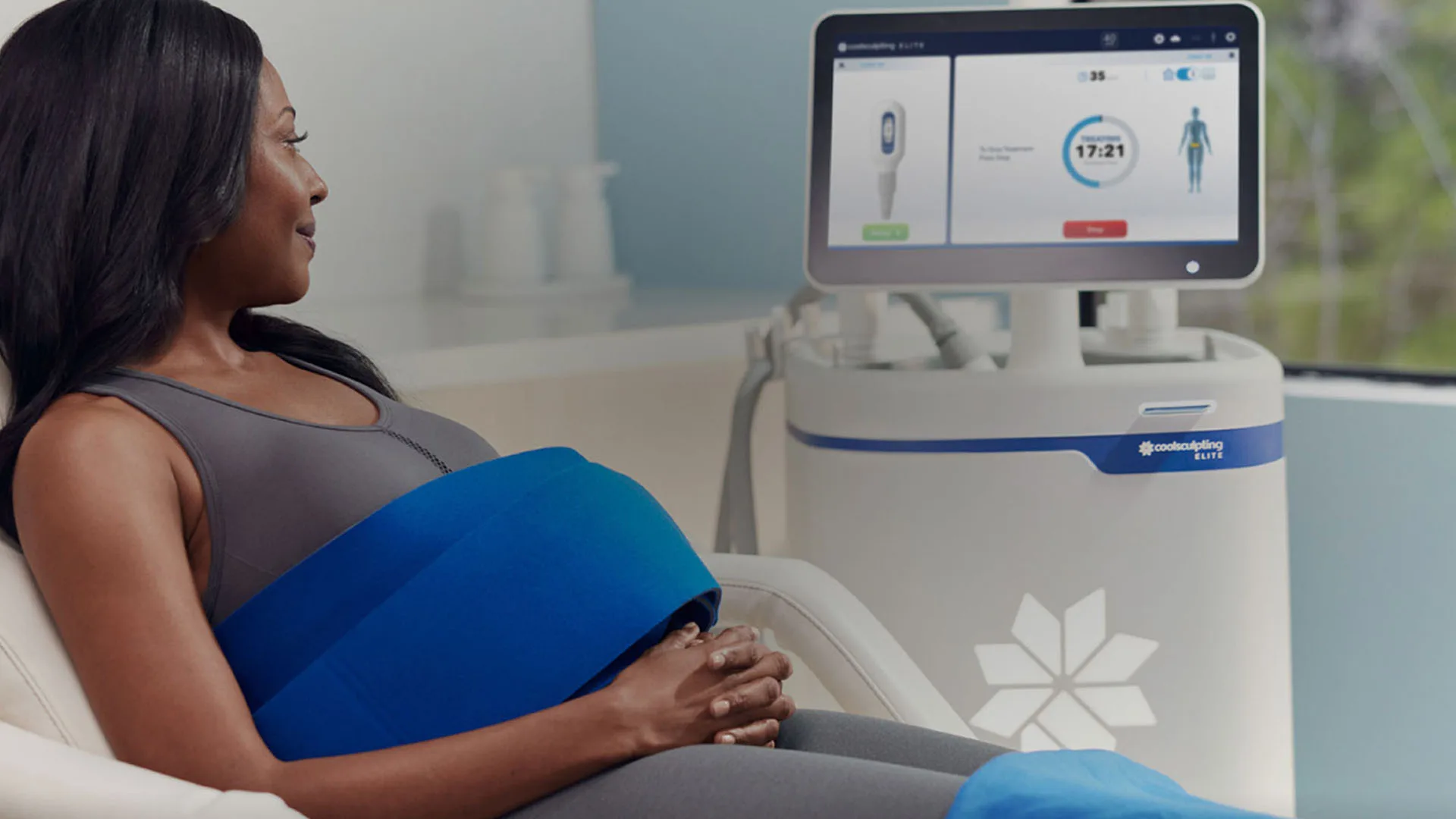 Woman relaxing during a CoolSculpting Elite treatment beside the Elite system